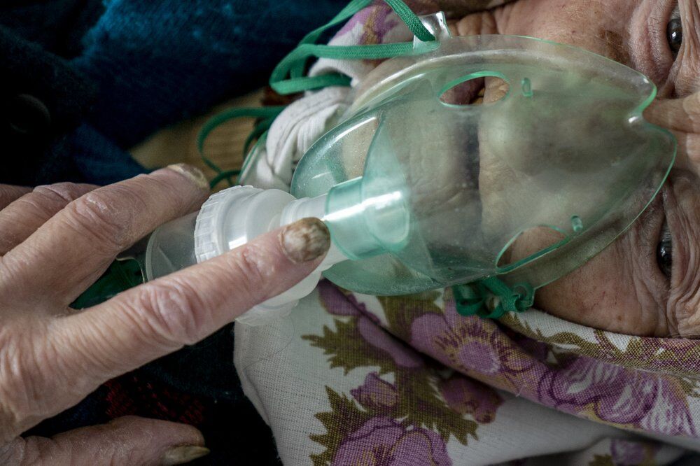 Пожилая женщина с коронавирусом дышит с помощью кислородной маски в больнице Почаева