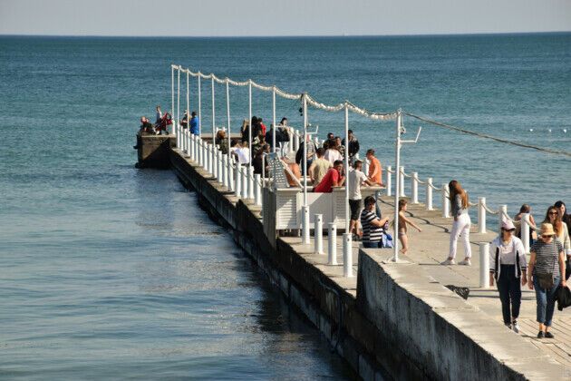 На хвилерізах біля моря люди гуляють групами.