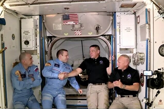 Сотрудники МКС встречают двух астронавтов Crew Dragon. На стене на заднем плане – флаг США