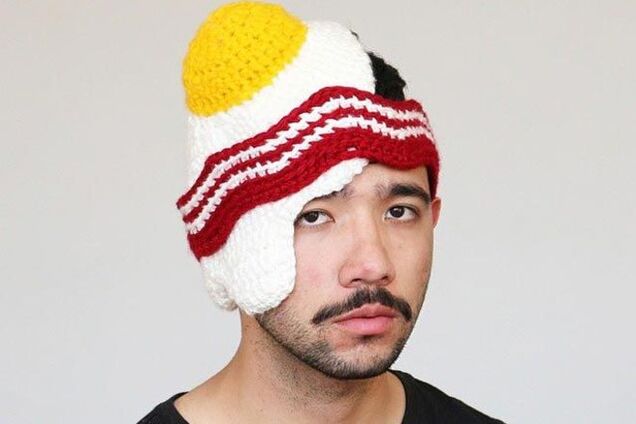 Парень вяжет шляпы, похожие на продукты и носит их с грустным лицом