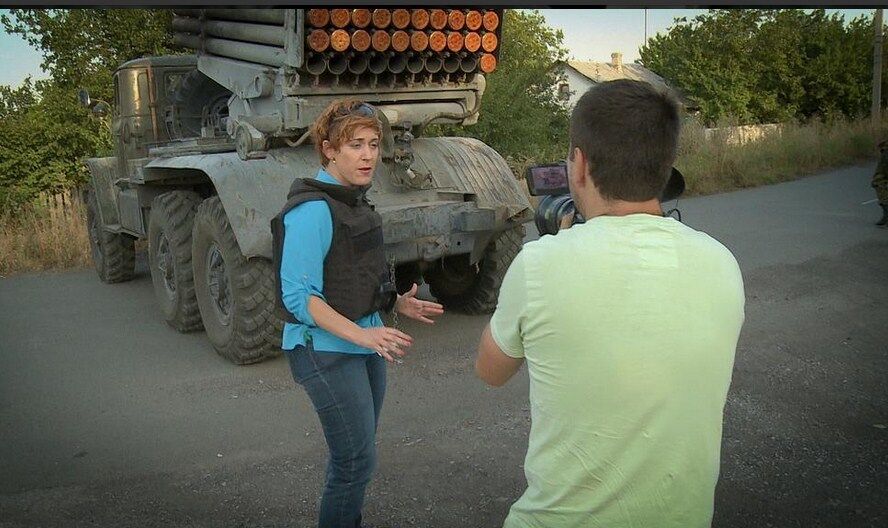 Журналистка RussiaToday с улыбкой позирует на фоне стреляющего "Града"