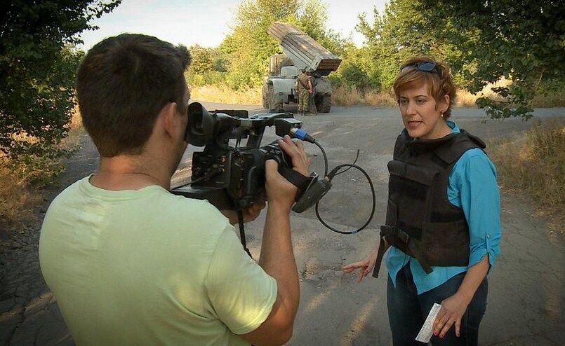Журналистка RussiaToday с улыбкой позирует на фоне стреляющего "Града"