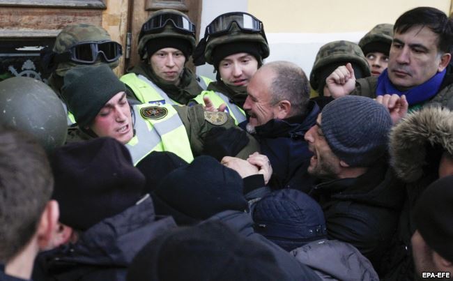 Міхеїл Саакашвілі (праворуч) спостерігає, як мітингувальники, яких він закликав йти до Жовтневого палацу, під час штурму будівлі виривають бійця Нацгвардії зі строю перед центральним входом до будівлі. Київ, 17 грудня 2017 року