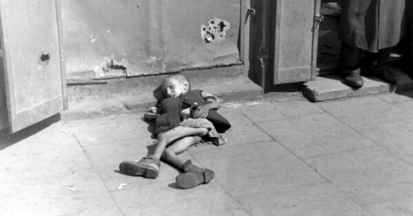 Истощенный ребенок, лежащий на тротуаре в варшавском гетто