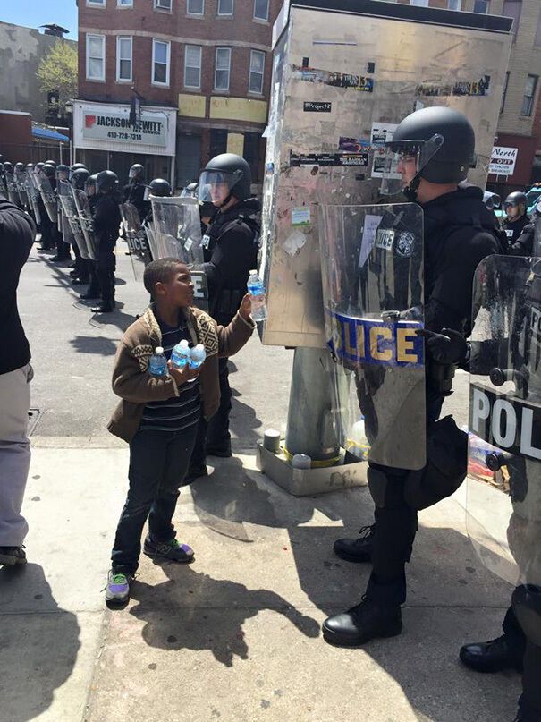 Мальчик предлагает бутылку воды полицейскому.
