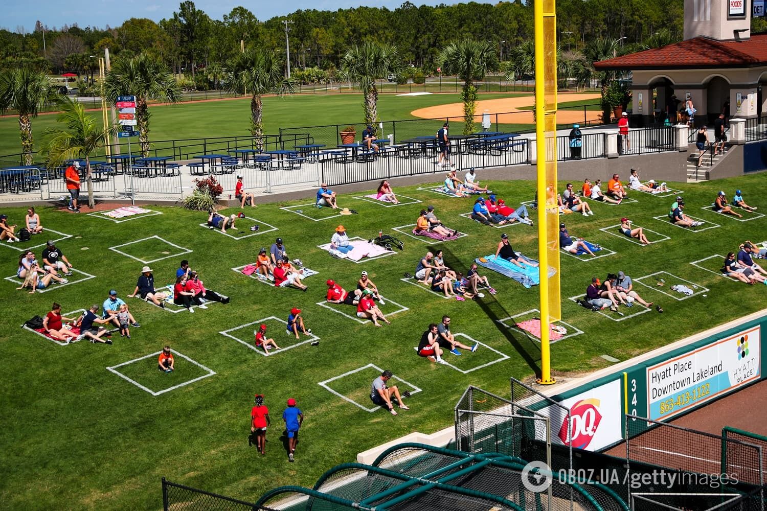 Поклонники сидели в социальных прямоугольниках, нарисованных на траве за левым полем во время весенних тренировочных игр по американскому футболу на стадионе Detroit Tigers в Лейкленде, штат Флорида