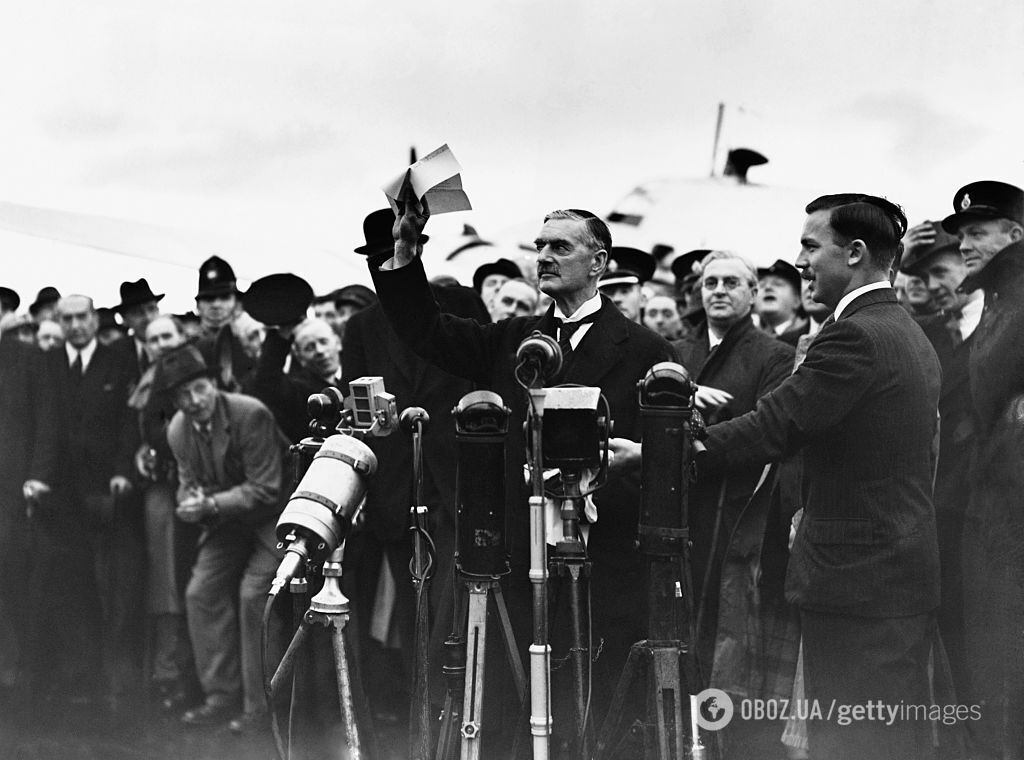 Премьер-министр Невилл Чемберлен машет толпе в аэропорту Хестон и заявляет: "Мир в наше время", по возвращении после подписания Мюнхенского соглашения.