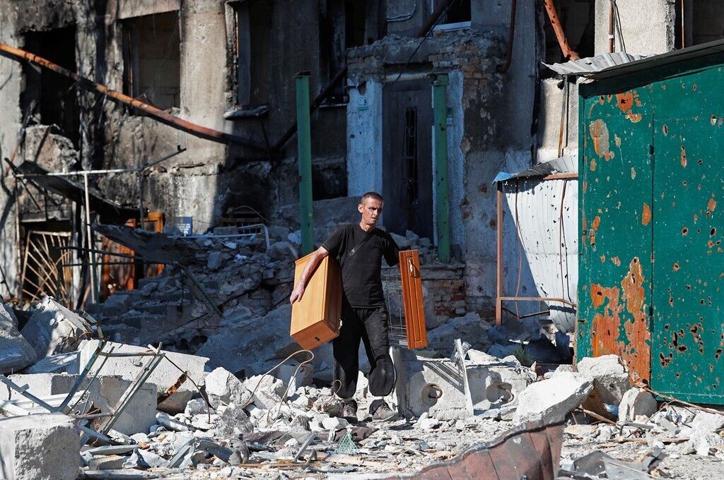 Мужчина вывозит мебель из разрушенного жилого дома
