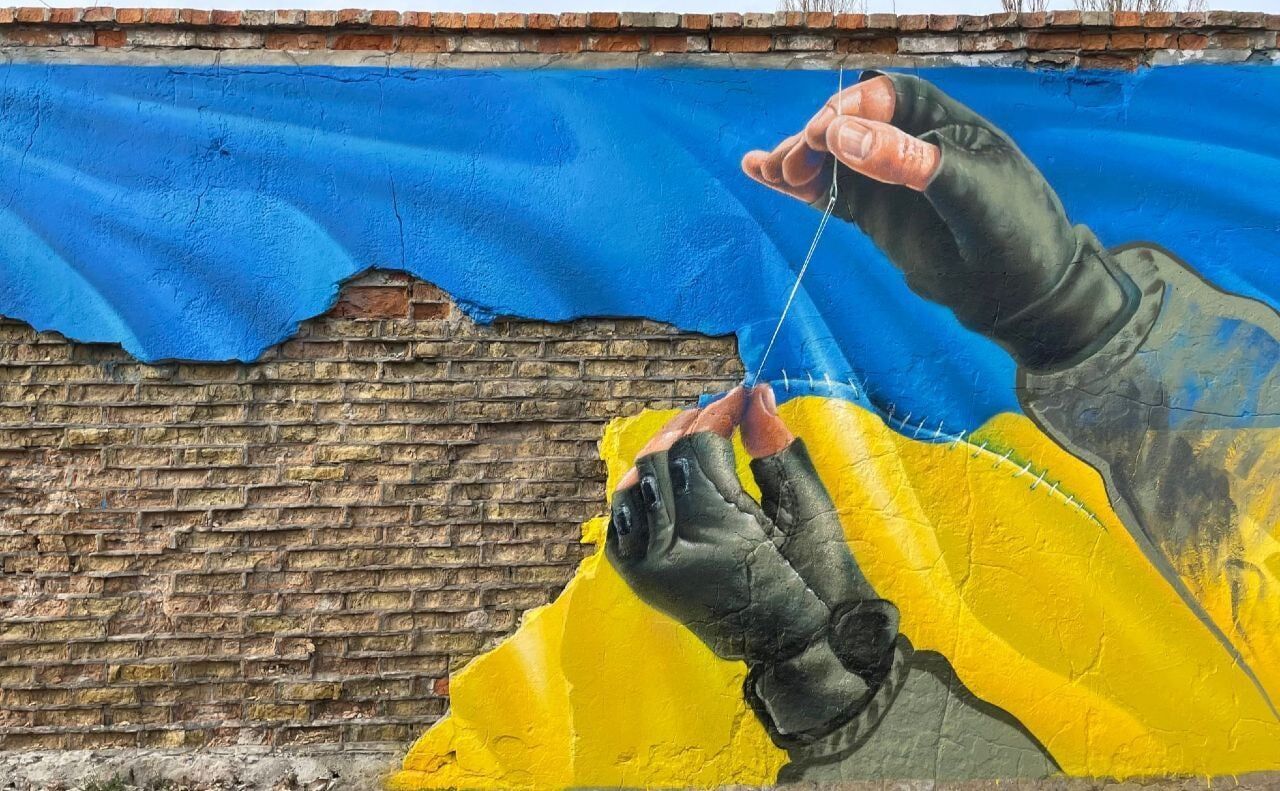 Украинский защитник сшивает разорванный флаг Украины.