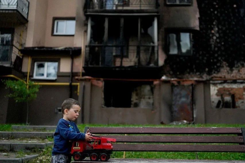 Дитина на тлі обгорілого будинку