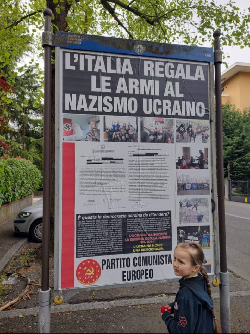 Дівчинка біля плакату із статтею: "Італія дарує зброю українському нацизму".