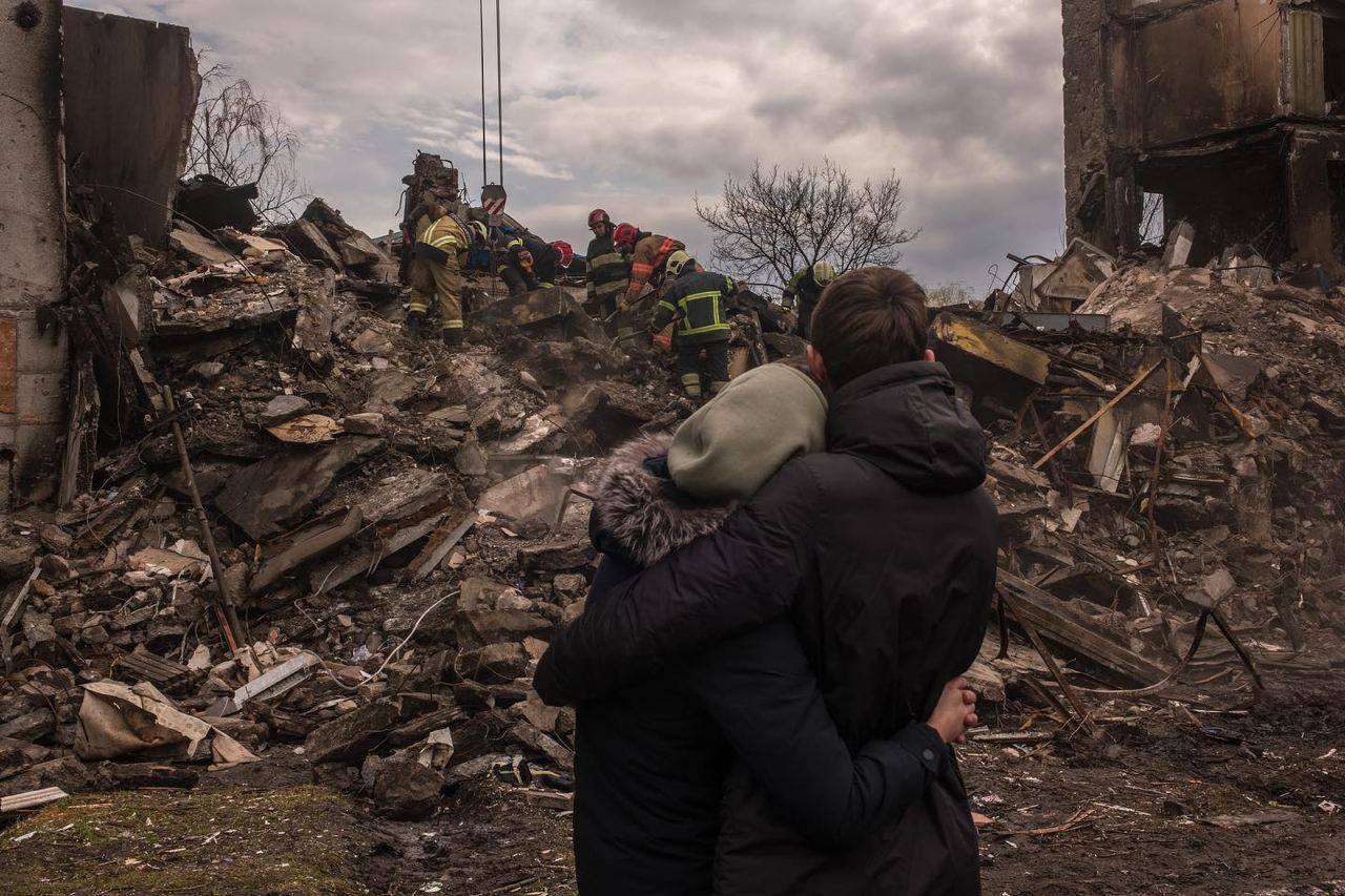 Люди обнимаются на фоне развалин дома