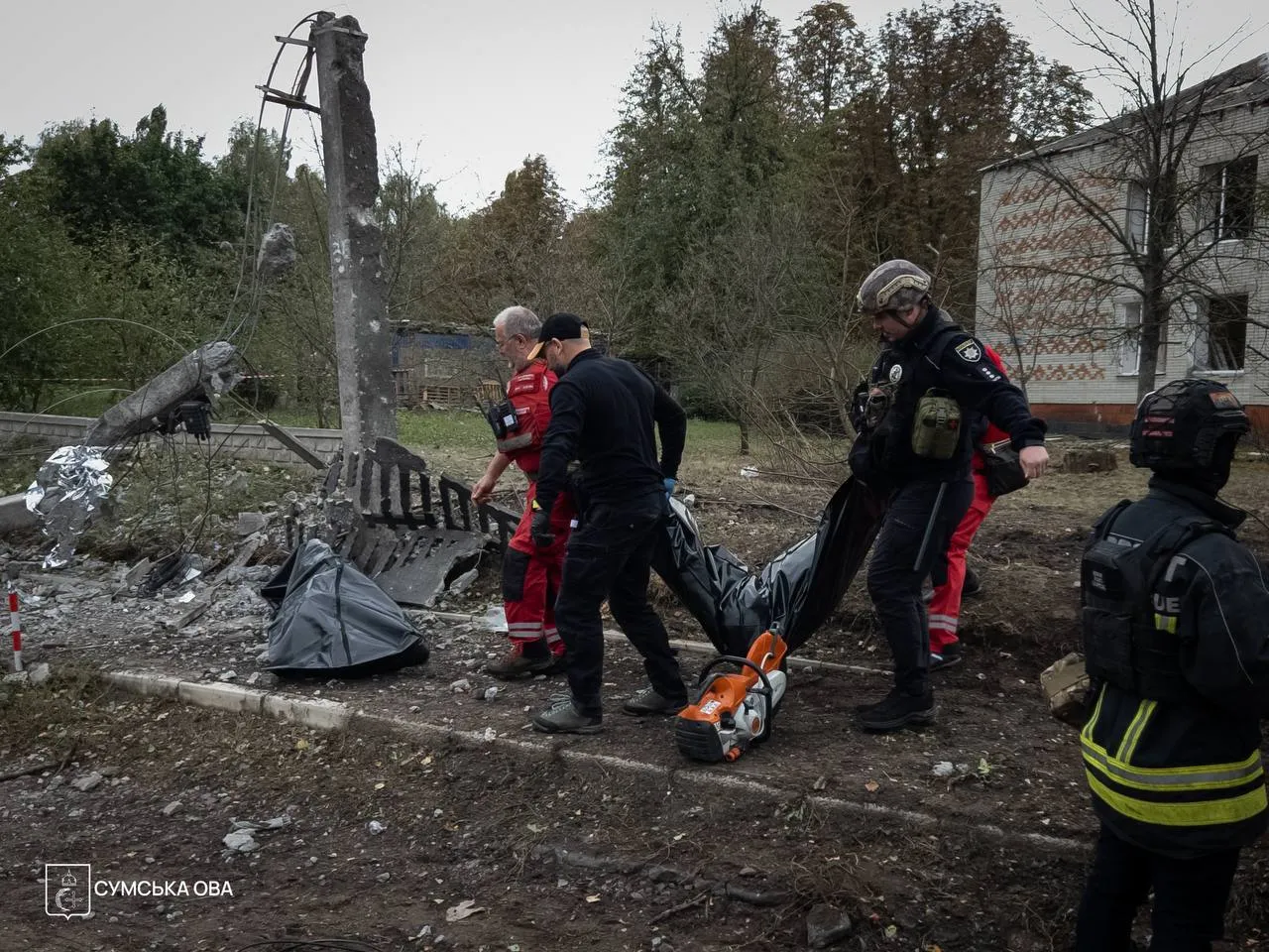 Спасатели несут тело погибшей в результате российского удара по Сумам.