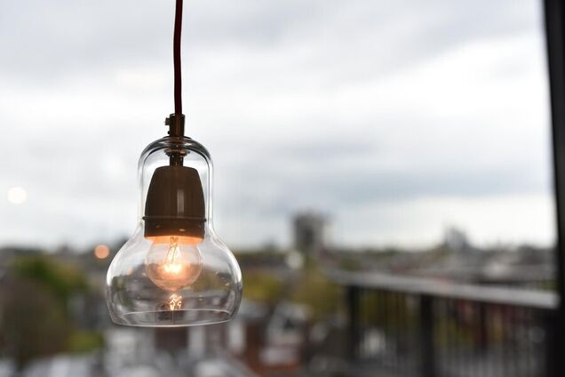 Электрическая лампа на фоне города. Иллюстрация к отключениям электроэнергии