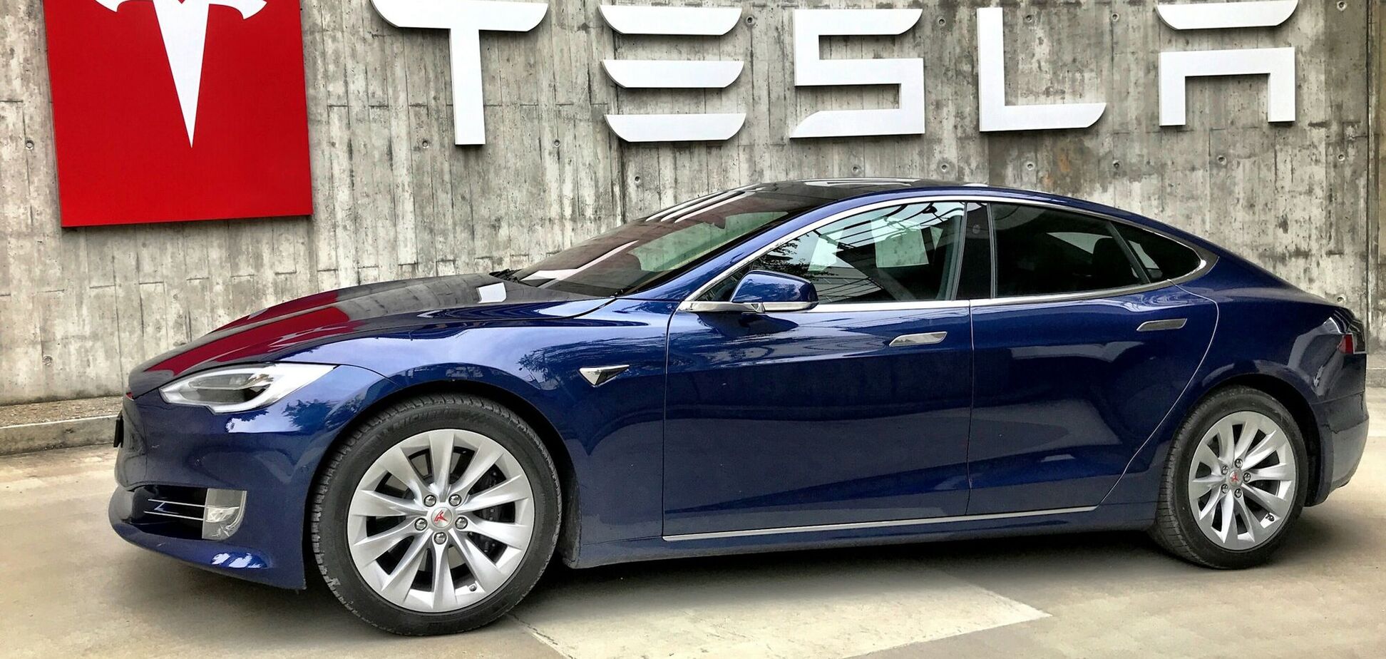 Иллюстрация - электрокар Tesla на фоне вывески компании