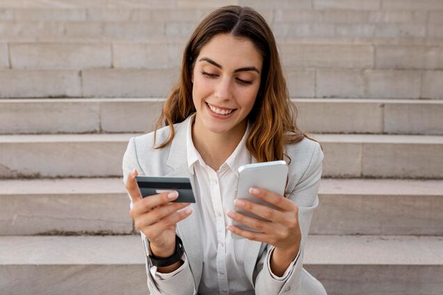 Иллюстрация - девушка держит в руках банковскую карточку и смартфон